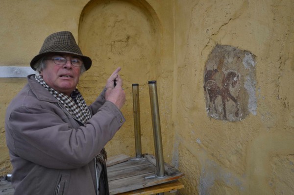 Anton Socaci indică locul unde de sub tencuială răzbate pictura cu zeul dac